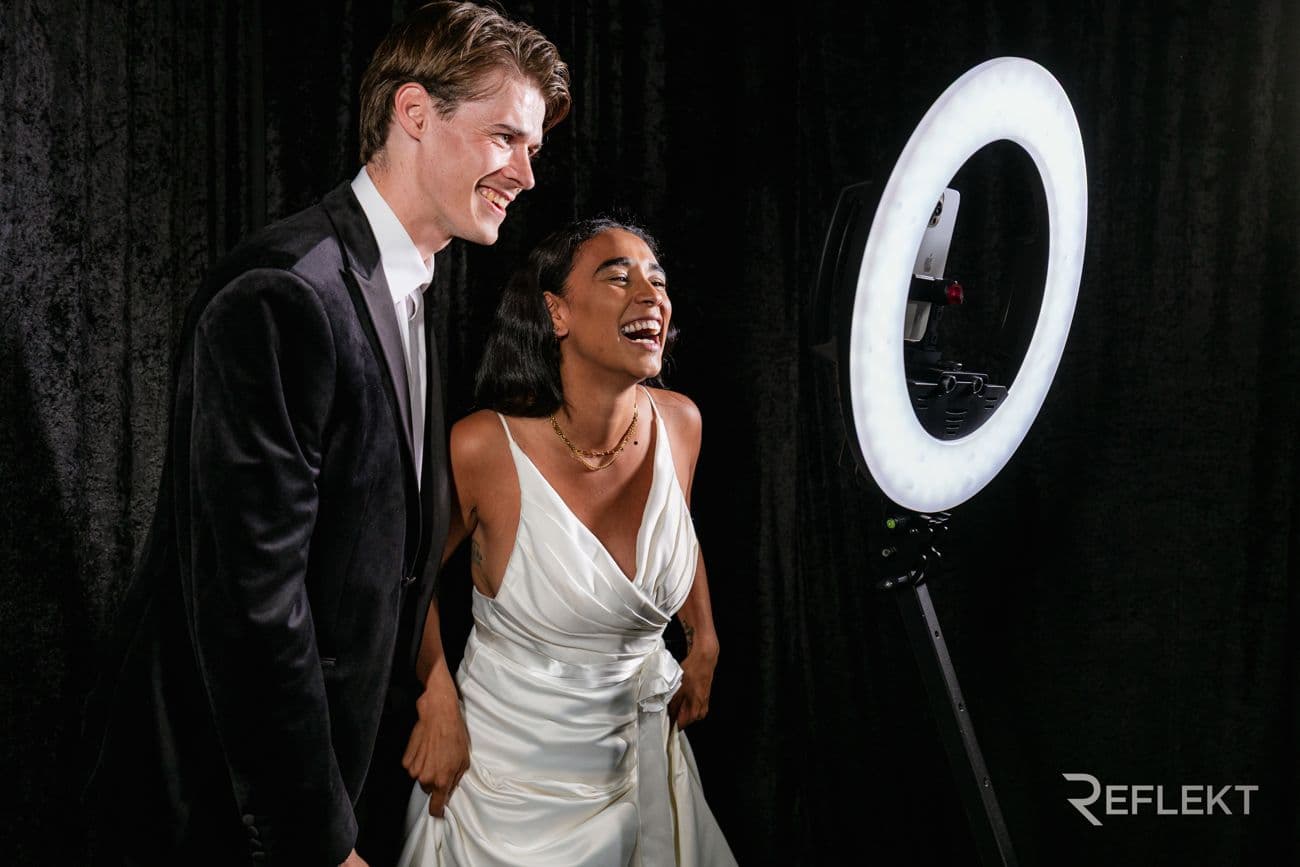 Couple laughing in front of a ring-light photo booth at a wedding