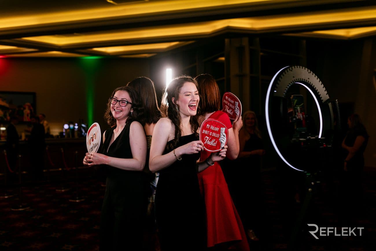 Guests posing with props in front of a ring-light photo booth at an evening event