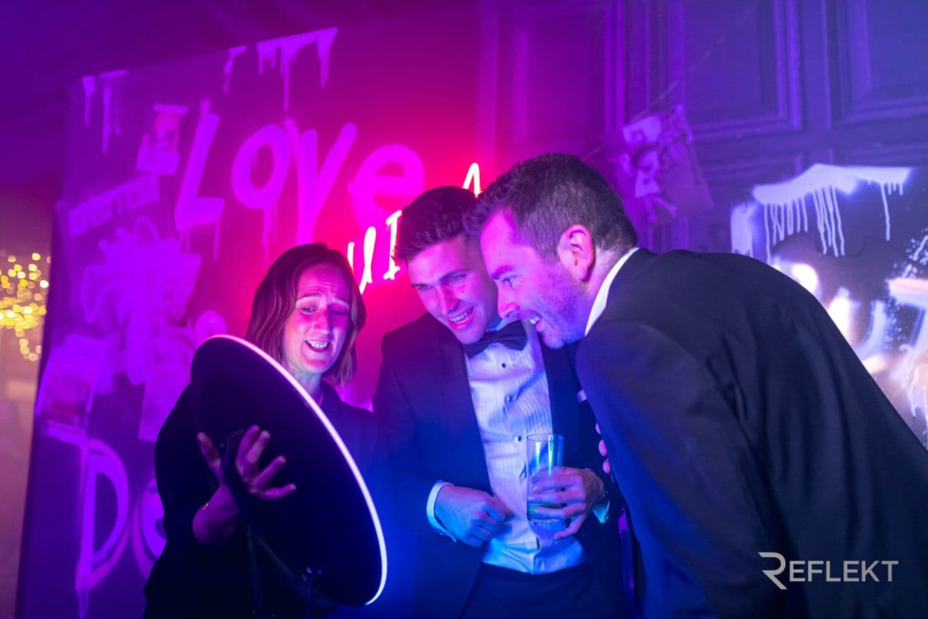 Guests in formal wear checking their photo on a roaming photo booth at a party